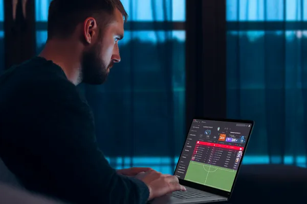 KKFBB মোবাইল অ্যাপ — ক্যাসিনো ও স্পোর্টসের সম্পূর্ণ হাব একজন পুরুষ তার ল্যাপটপে মনোযোগ দিয়ে কাজ করছেন, ব্যাকগ্রাউন্ডে লাইভ স্ট্যাটস — যা KKFBB মোবাইল অ্যাপের স্পোর্টস ও গেমিং ফিচারগুলোকে তুলে ধরে।