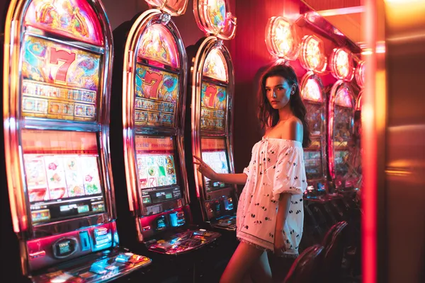 KKFBB Slots — Thousands of exciting themes and jackpots A stylish woman beside vibrant slot machines displaying glowing sevens, showcasing the variety of top slots at KKFBB.